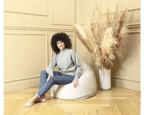 Kvinna sitter på en ljus sittpuff i ett rum med torkade blommor i en vas.