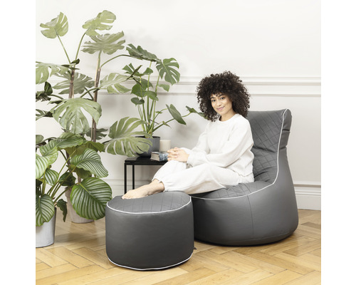 Kvinna sitter i en grå fåtölj med fotpall framför växter