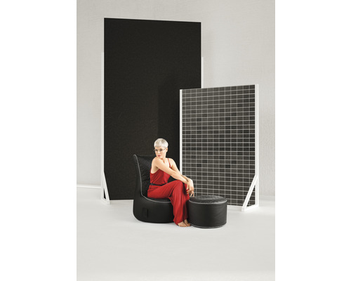 Kvinna sitter på en svart fåtölj med fotpall framför dekorativa paneler