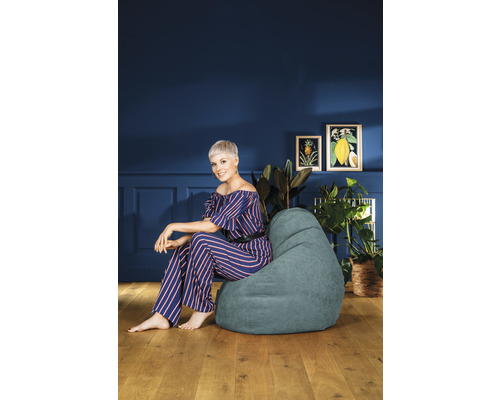 Kvinna sitter i ett rum på en sittsäck, omgiven av krukväxter och bilder.