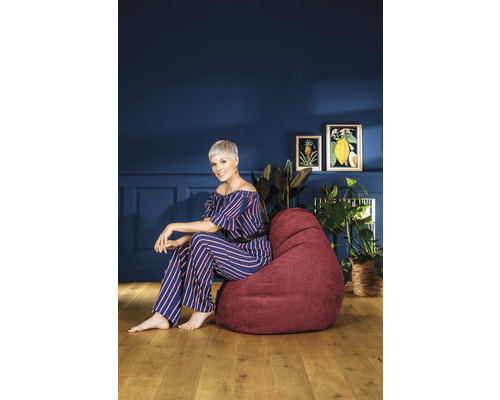 Kvinna sitter på en vinröd sittsäck i vardagsrummet framför en blå vägg med dekoration