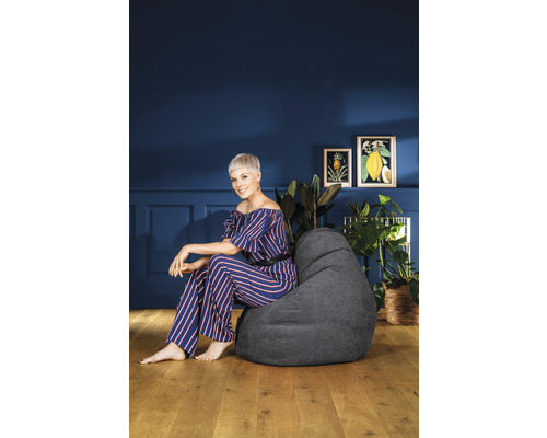 Kvinna sitter på en grå sittsäck i ett vardagsrum med växter och tavlor