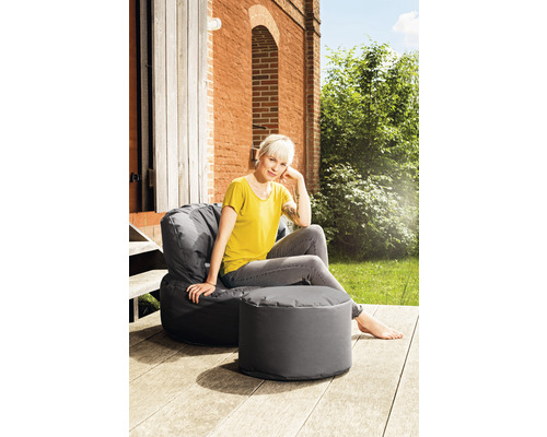 Kvinna sitter i en grå sittsäck med fotpall utomhus