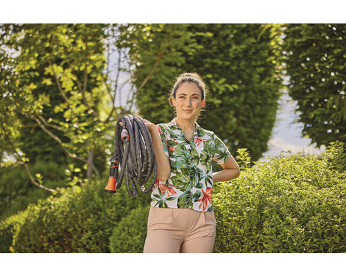 Kvinna håller en trädgårdsslang i en trädgård.