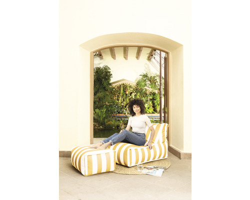 Kvinna sitter i ett rum på en randig sittsäck med fotpall