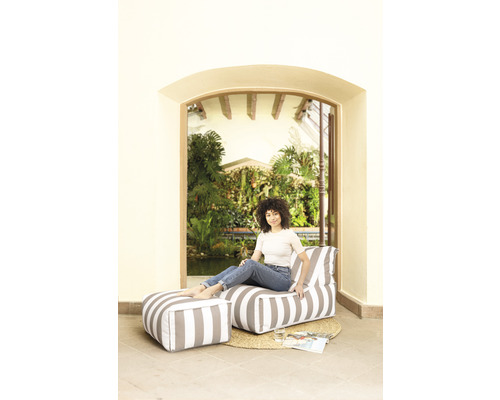 Kvinna sitter på en randig loungestol med fotpall i trädgården