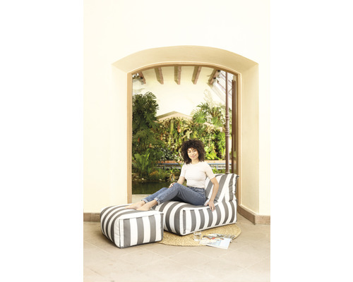 Kvinna sitter på en randig sittsäck med fotpall framför en trädgårdsscen