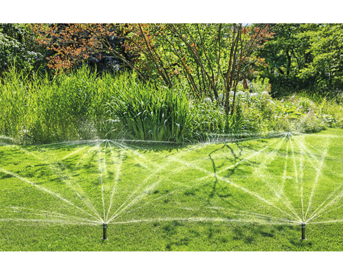 Grässpridare vattnar en gräsmatta i en trädgård.