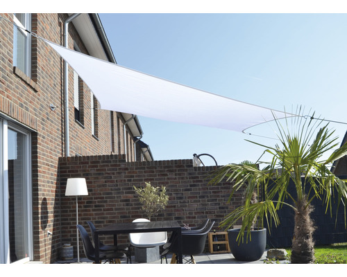 Terrass med solsegel, bord och stolar framför en tegelbyggnad
