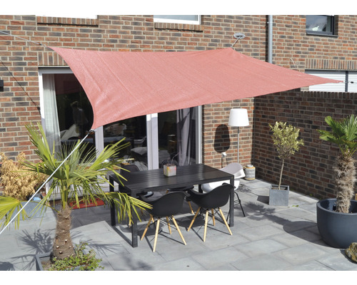 Terrass med solsegel, bord och stolar framför tegelbyggnad