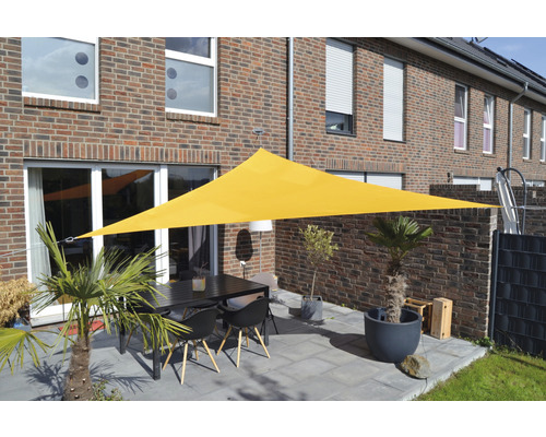 Gul, trekantig solsegel över en terrass med bord och stolar framför ett bostadshus.