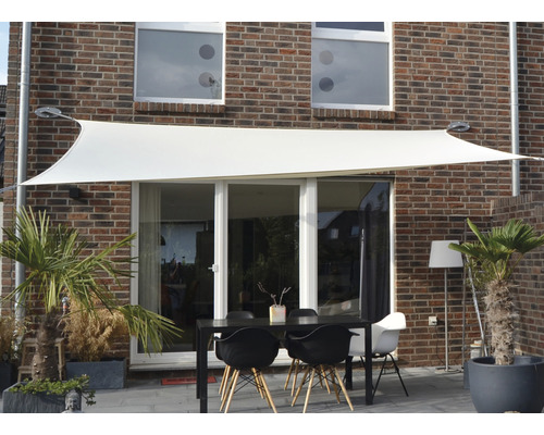 Scen med solsegel ovanför ett trädgårdsbord framför ett hus