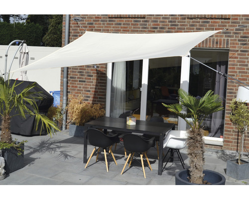 Uteplats med solsegel, trädgårdsbord och stolar framför en husvägg