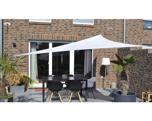 Terrass med solsegel, bord och stolar framför ett tegelhus