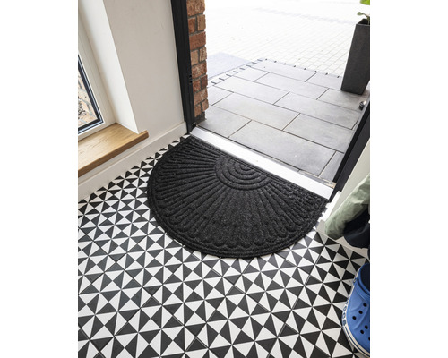 Halvrund dörrmatta i textil framför en ytterdörr på ett golv med geometriskt mönster