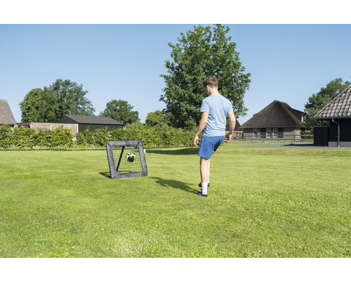 Person spelar fotboll med ett fotbollsmål i trädgården.