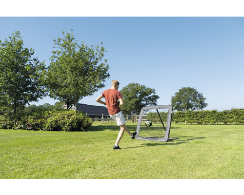 Pojke sparkar fotboll i ett portabelt fotbollsmål i trädgården.