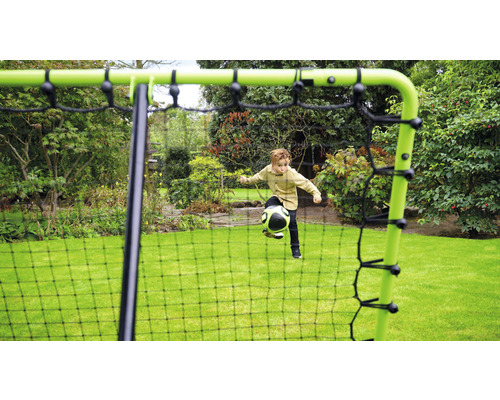Pojke leker med en boll framför ett fotbollsmål i trädgården.