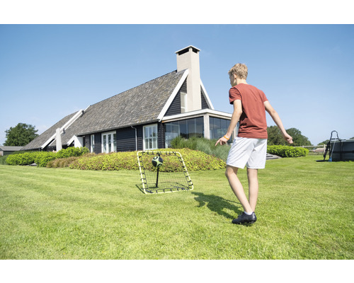 Pojke leker med fotbollsmål i trädgården framför ett bostadshus