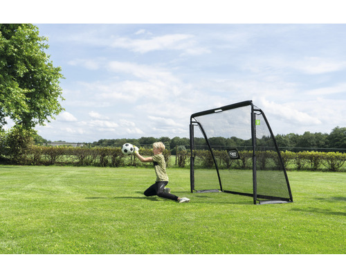 Utomhusscen med ett fotbollsmål och en målvakt som fångar en boll på en gräsmatta.