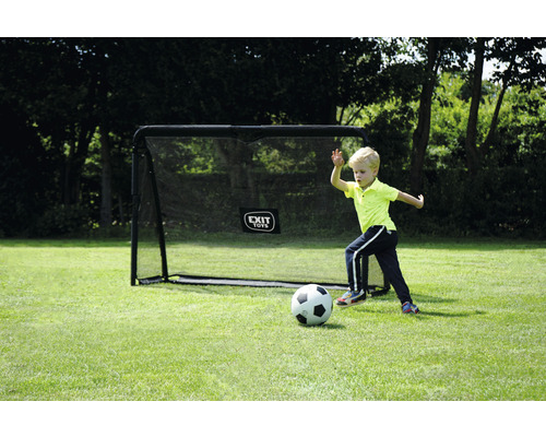 Pojke spelar fotboll framför ett fotbollsmål i trädgården.
