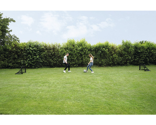 Två personer spelar fotboll på en gräsmatta med två fotbollsmål.