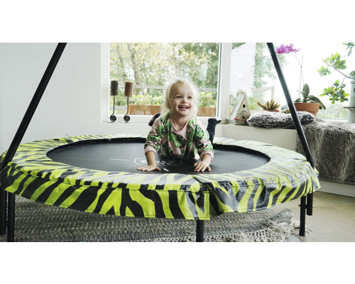 Ett barn ligger och skrattar på en rund studsmatta med djurmönster inomhus.