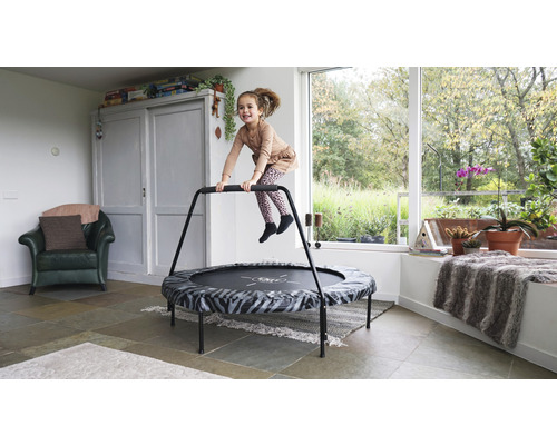 Flicka hoppar på en fitnesstudsmatta med handtag i ett ljust rum.