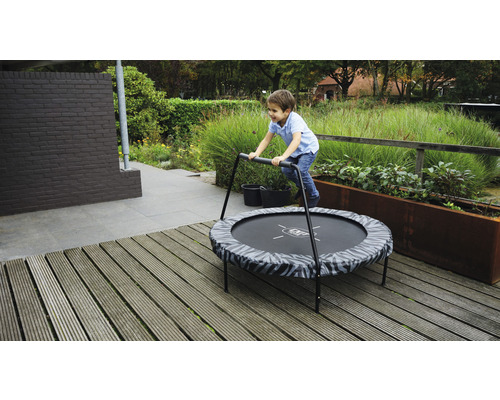 Pojke hoppar på en rund trädgårdstrampolin med handtag