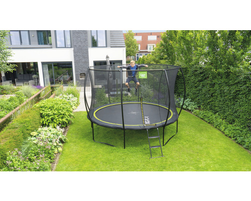 Pojke hoppar på en trädgårdstrampolin med säkerhetsnät och stege framför ett bostadshus.