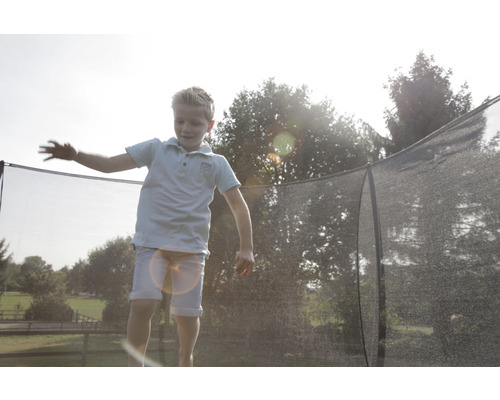 En pojke hoppar på en trädgårdstrampolin med säkerhetsnät.