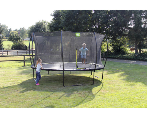 Trampolin med säkerhetsnät i trädgården med lekande barn