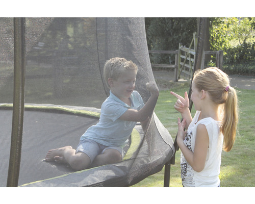 Två barn leker på en trädgårdstrampolin med säkerhetsnät.
