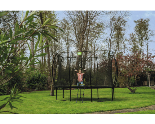 Barn på en studsmatta med säkerhetsnät och stege i trädgården.