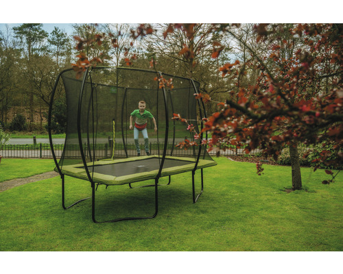 Pojke hoppar på rektangulär trädgårdstrampolin med säkerhetsnät på gräsmatta.