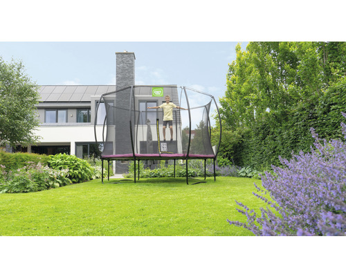 En pojke hoppar på en rektangulär trädgårdstrampolin med skyddsnät framför ett hus.