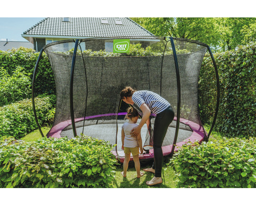 Trädgårdsscen med en studsmatta med säkerhetsnät, en kvinna och ett barn.