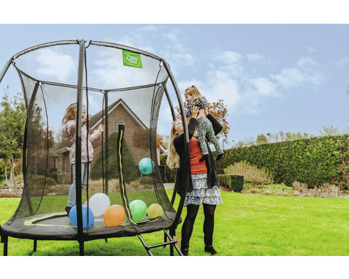 Trampolin med säkerhetsnät i trädgården med lekande barn och en kvinna som bär ett barn på sina axlar