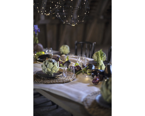 Festligt dukat bord med sfäriska ljusslingor, porslin, glas och säsongens grönsaker som dekoration.