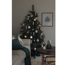 Julgran dekorerad med kulor och ljus bredvid en soffa och ett bord