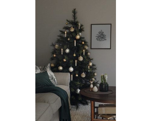 Julgran dekorerad med kulor och ljus bredvid en soffa och ett bord