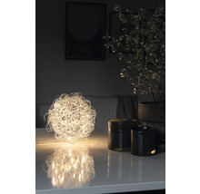 Dekorativ bordslampa i form av ett klot bredvid ljus och krukväxt på bordet