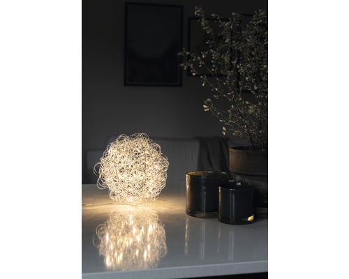 Dekorativ bordslampa i form av ett klot bredvid ljus och krukväxt på bordet