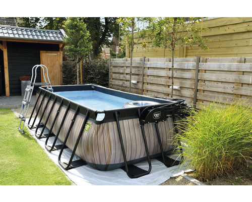 Rektangulär pool med träpanel, stege och filterpump i trädgården.