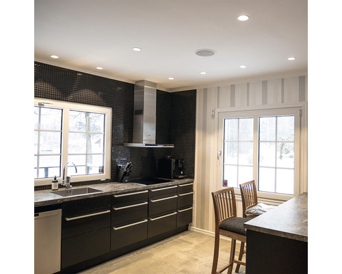 Kök med diskho, spis, köksfläkt, taklampor och sittplatser vid en köksbänk