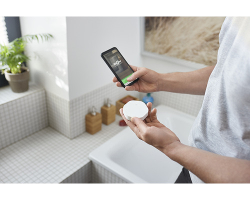 En person håller en WiZ-sensor och en smarttelefon i ett badrum.