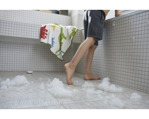 Ett barn står i badrummet med ett badkar, en handduk och badskum på golvet.