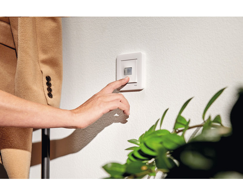 En person trycker på en rörelsedetektor på en vägg.