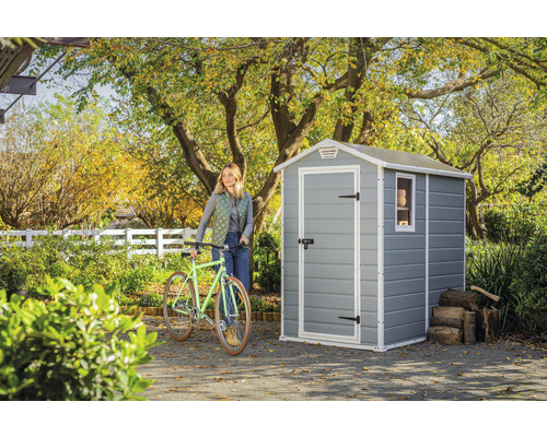 Trädgårdsscen med trädgårdsskjul, cykel och kvinna i trädgården