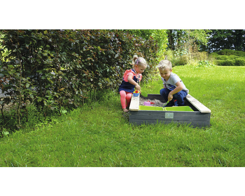 Barn leker i en sandlåda med gröna behållare i trädgården.